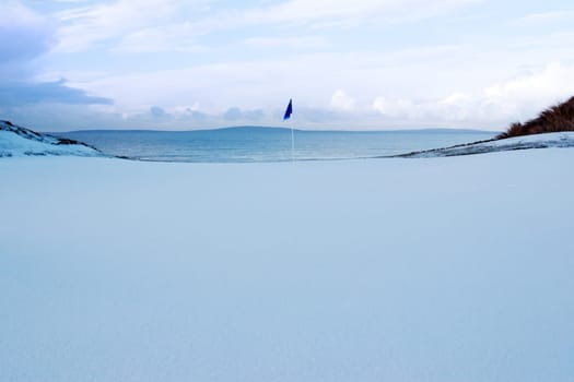 a snow covered links golf hole in ireland in winter weather with blue flag