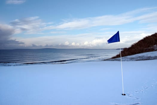 a snow covered links golf hole in ireland in winter weather with blue flag