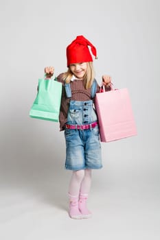 Studio portrait of happy smiling young girl with red Christmas hat carrying Christmas shopping bags