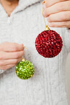 Closeup of red and green Christmas baubles hanging from fingers