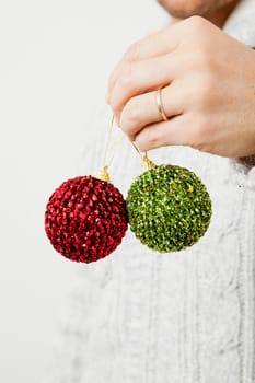 Closeup of green and red Christmas baubles held my man wearing gold wedding ring