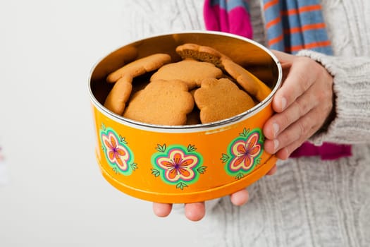 Tin of gingerbread biscuits being held up and presented by man wearing scalf