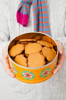 Tin of gingerbread biscuits being held up and presented by man wearing scalf