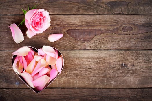 Rose petals as a heart on wooden board