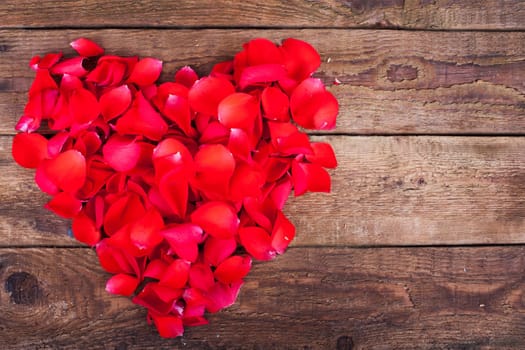 Rose petals as a heart on wooden board