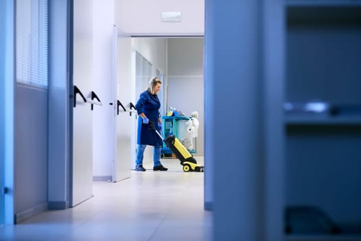 Woman working, professional maid cleaning and washing floor with machinery in industrial building