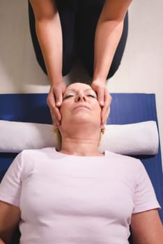 Alternative traditional medicine and massage, young spirit healer doing reiki treatment to old woman. High angle view, head and shoulders