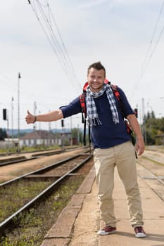Man hitchhiking on railroad train station smiling backpack travel tourist
