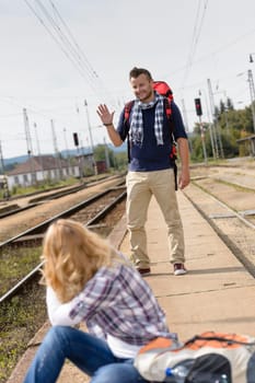 Man waving to woman sitting on railroad vacation travel backpack