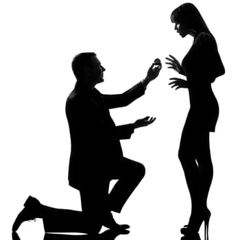 one caucasian couple man kneeling offering engagement ring and woman surprised in studio silhouette isolated on white background