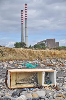 Trashed fridge on the seashore next to a factory