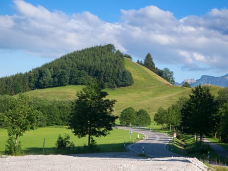 View along a winding country road in the Allgäu near the town of Pfonten with a hill in the center