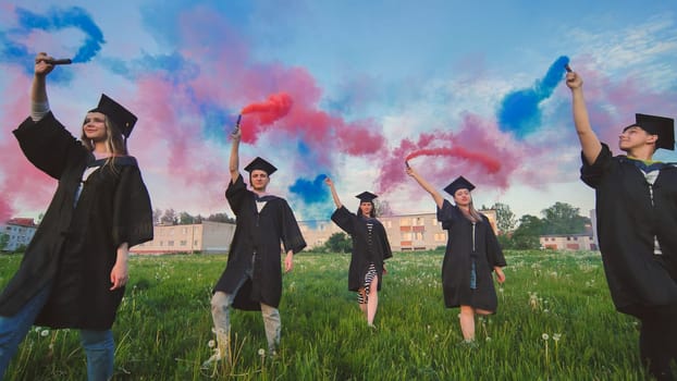 Students graduate with colored smoke walking through the meadow in the evening