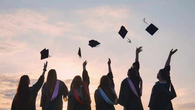 Student graduates toss their caps at sunset