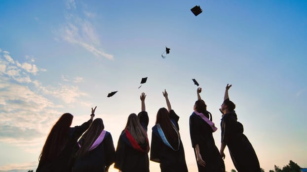 Student graduates toss their caps at sunset