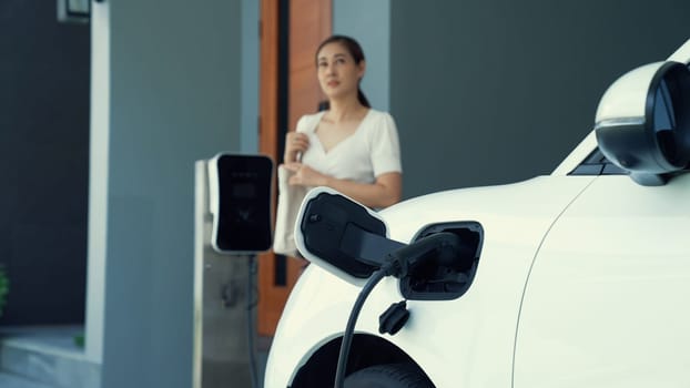 A woman unplugs the electric vehicle's charger at his residence. Concept of the use of electric vehicles in a progressive lifestyle contributes to a clean and healthy environment.