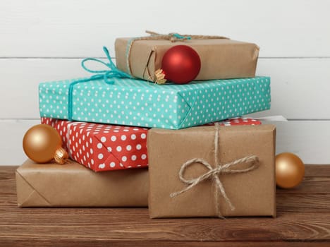 Close up stack of several red and brown paper wrapped Christmas gifts on wooden table over white wall