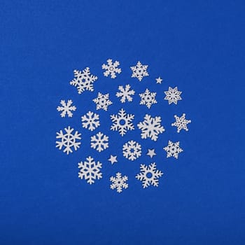 Close up circle of white wooden snowflakes Christmas decoration over blue felt background, table top view, flat lay