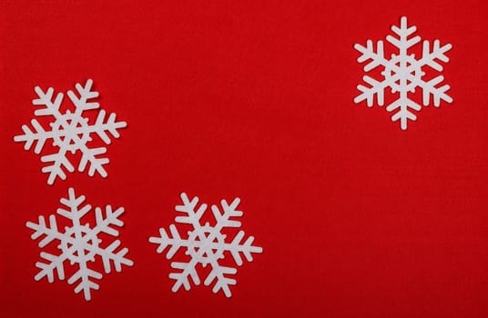 Close up pattern of white felt snowflakes Christmas decoration over red background, table top view, flat lay