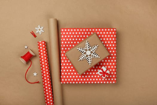 Close up flat lay of packing and wrapping Christmas gift boxes with red paper, table top view, directly above