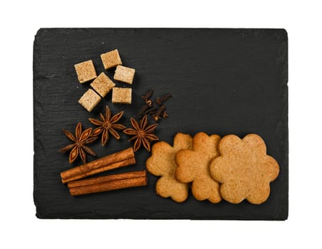 Close up gingerbread cookies with cinnamon, cloves and star anise spices on black slate with copy space isolated on white background, elevated top view, directly above