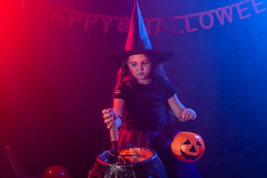 Little witch child cooking potion in the cauldron on Halloween