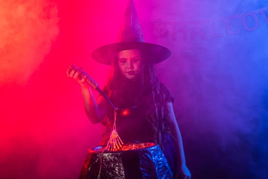 Child girl witch preparing a potion in the cauldron at halloween holidays