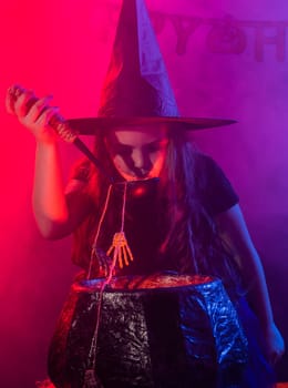 Child girl witch preparing a potion in the cauldron at halloween holidays