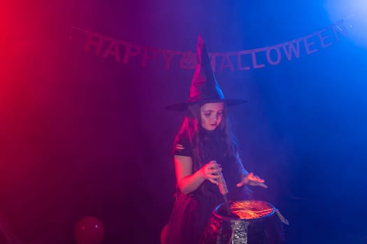 Little witch child cooking potion in the cauldron on Halloween