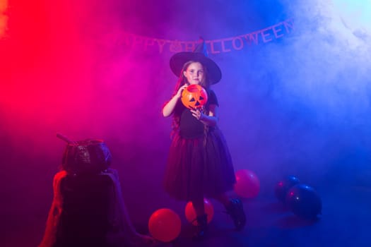 Funny child girl in witch costume for Halloween with pumpkin Jack