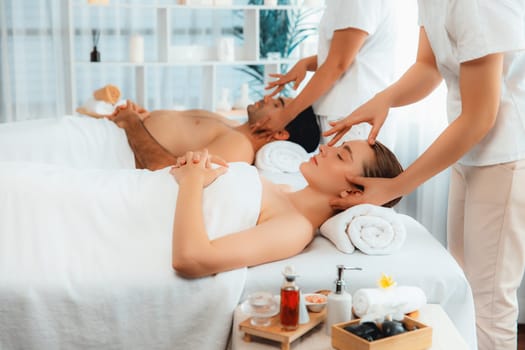 Caucasian couple enjoying relaxing anti-stress head massage and pampering facial beauty skin recreation leisure in dayspa modern light ambient at luxury resort or hotel spa salon. Quiescent