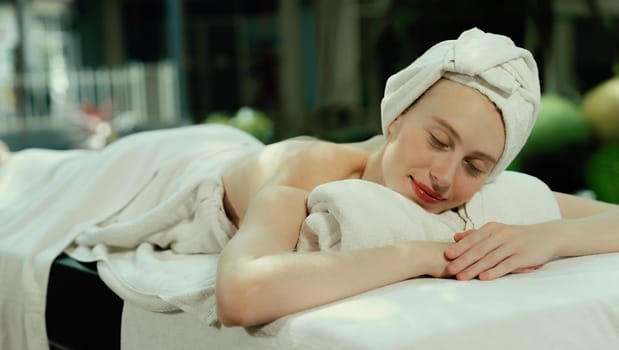 Beautiful young woman relaxes on a spa bed surrounded by nature. ready for a body massage. Attractive female in white towel lying peacefully during waiting for body massage. Close up. Tranquility