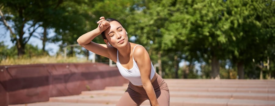 Portrait of sportswoman panting, taking break during jogging training, sweating while running outdoors.