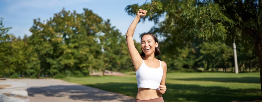 Hooray, victory. Smiling asian girl triumphing, celebrating achievement, running till finish, shouting from excitement.