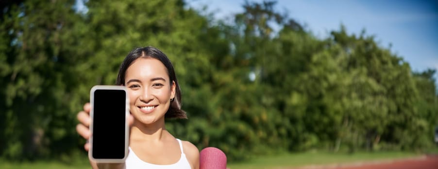 Vertical shot of fit and healthy young asian woman, shows smartphone screen with her workout stats, recommends telephone application.