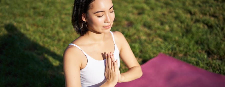 Portrait of young mindful woman, practice yoga, exercising, inhale and exhale on fresh air in park, sitting on rubber mat.