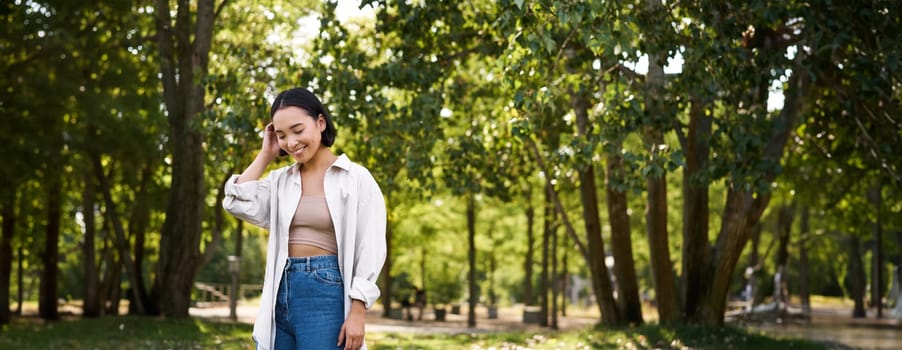 Image of korean girl walking in park, smiling while having a mindful walk in woods.
