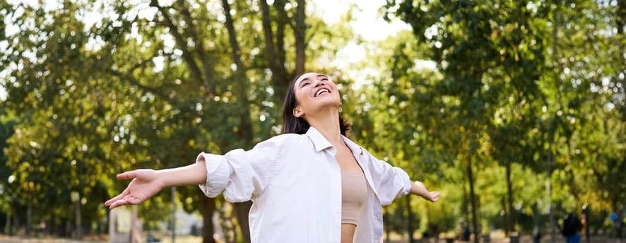 Portrait of carefree young asian woman dancing in park alone, enjoying freedom, smiling with joy. Copy space