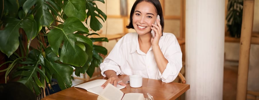 Smiling woman talking on mobile, answer phone call and looking happy, sitting in cafe. People and lifestyle concept