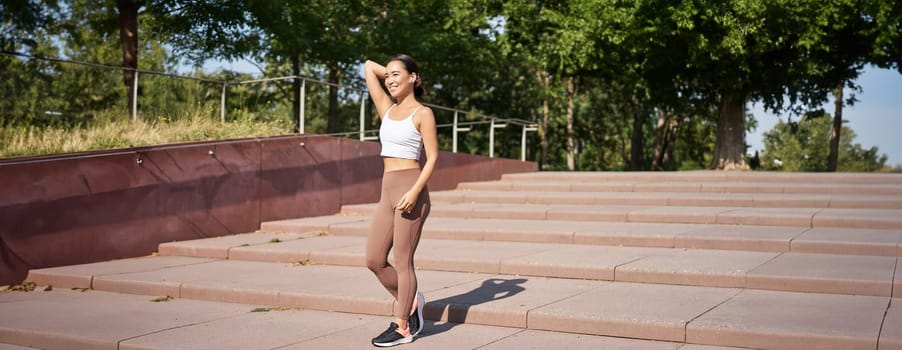 Portrait of young sportswoman running on street. Fitness girl jogging in park, workout outdoors, listening music in wireless earphones.