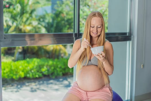 An expecting mother gracefully has breakfast on a fitness ball, illustrating the comfort it provides during pregnancy when traditional chairs may be less accommodating.