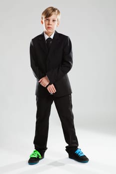 Studio portrait of serious looking young boy wearing black suit and colorful shoes