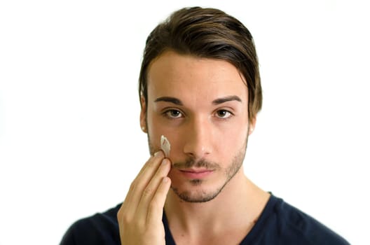 Attractive young man applying moisturizing cream or lotion on face skin