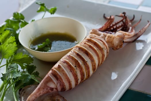 Grilled squid on white plate with knife and fork.