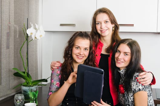 Three young women friends chatting at home and using laptop to look at new photo or browsing internet
