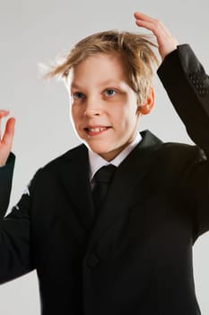 Studio portrait of happy smiling young boy in black suit with wind blowing hair