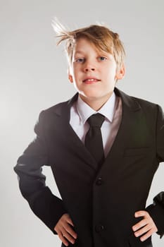 Studio portrait of smiling and relaxed young boy in black suit with wind blowing hair