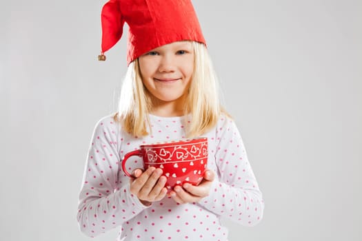 Studio portrait of happy young girl wearing red Christmas elf hat and holding a big red cup