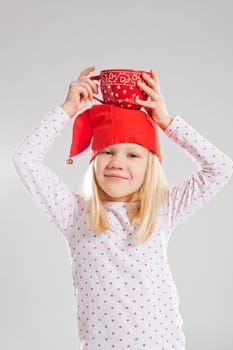 Studio portrait of smiling young girl wearing red Christmas elf hat holding big red cup on head