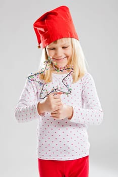 Studio portrait of smiling young girl wearing red Christmas elf hat and holding star decoration